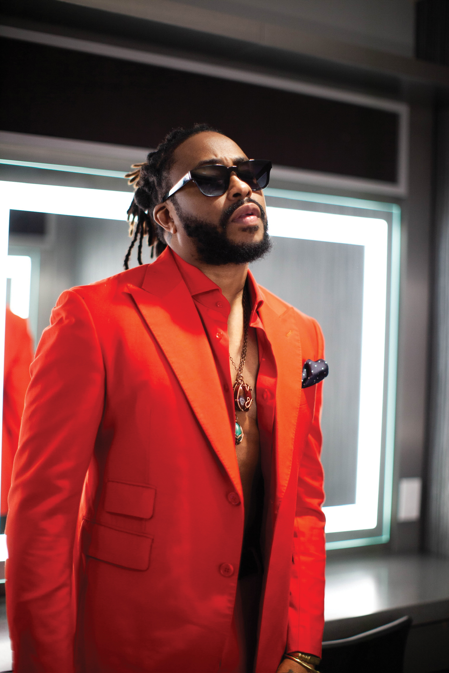 Raheem Devaughn wears a red suit in front of a lit mirror