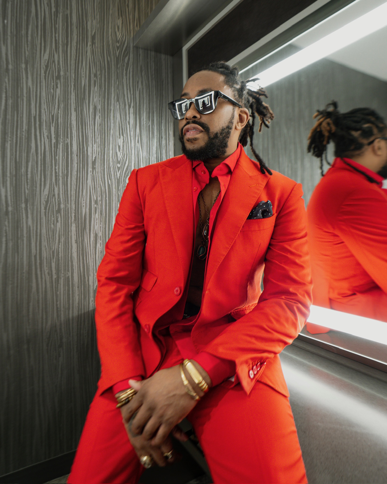 Raheem Devaughn wears a red suit in front of a lit mirror